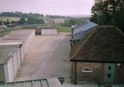 Rows of blue steel storage containers in a secure concrete yard in front of a warehouse